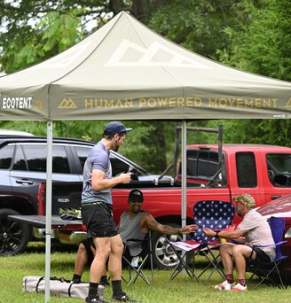 A group of men relaxing after a race under a green, printed Ecotent canopy tent.